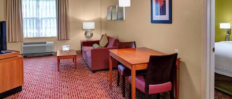 Habitación de hotel con alfombra roja estampada, un escritorio de madera, un sofá rojo, un televisor y una cama.