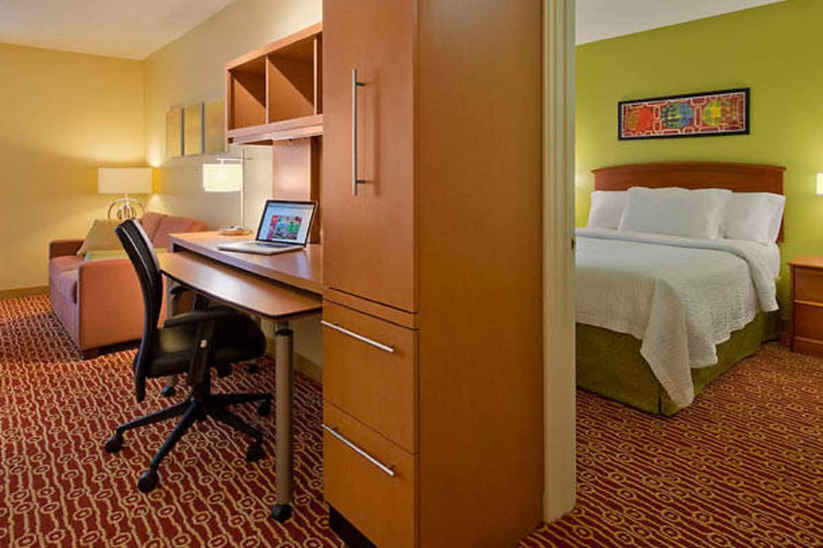 A hotel room with a desk, chair, bed, and a colorful painting on the wall.