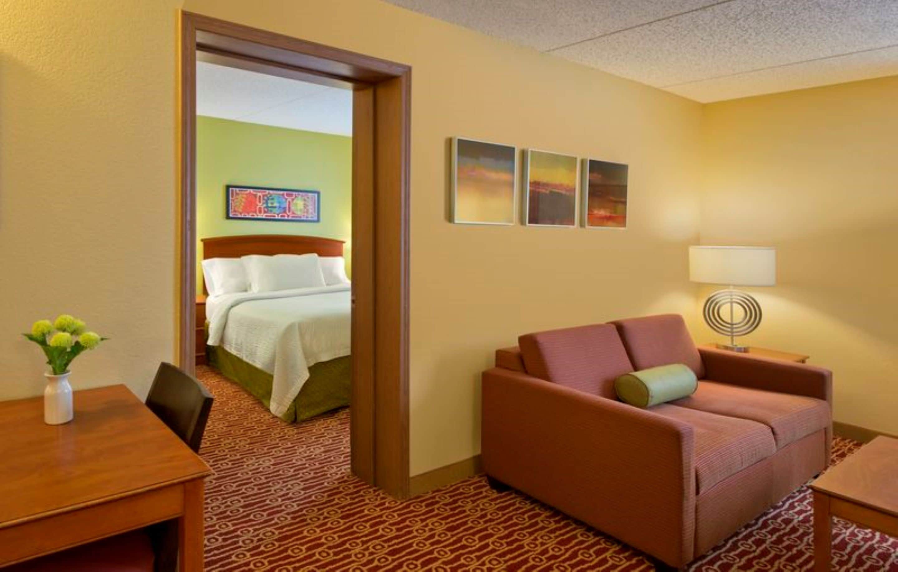 A hotel room with a bed, a sofa, a table, and a lamp.