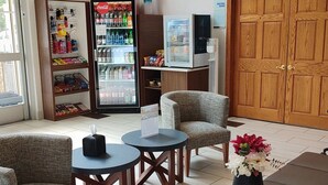 Een hotel lobby met zitplaatsen, een Coca-Cola koelkast, een bordje voor een vergaderruimte en een houten deur.