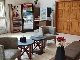 Un vestíbulo de hotel con asientos, un refrigerador de Coca-Cola, un letrero de sala de reuniones y una puerta de madera.