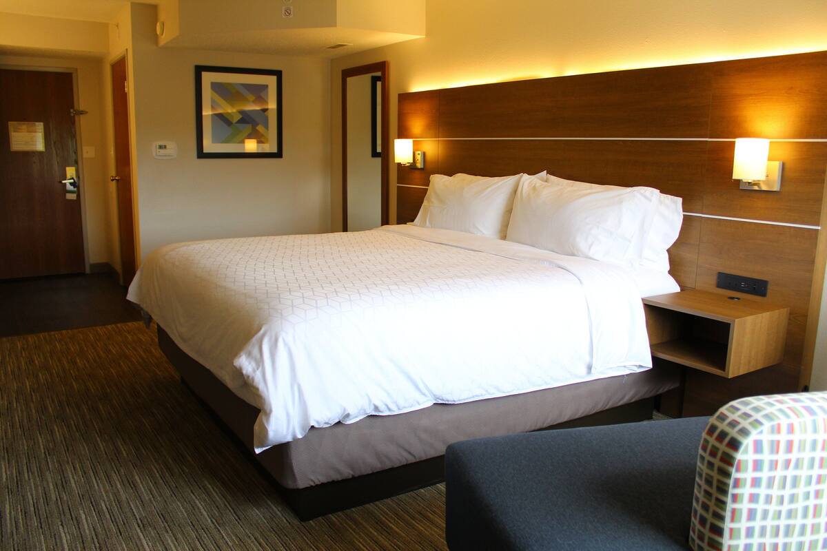Ein Hotelzimmer mit einem großen Bett, einem Nachttisch, einer Nachttischlampe und einer Wandleuchte.