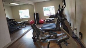 Een sportschool met trainingsapparatuur, een spiegelwand en ramen met uitzicht op buiten.