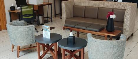 A modern lounge area with a sofa, two armchairs, and a small table with a sign.