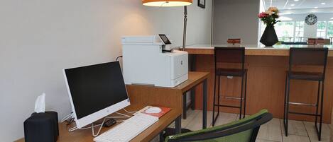 A workspace with a desktop computer, printer, and a lamp. There are two chairs and a small table with a vase of flowers.