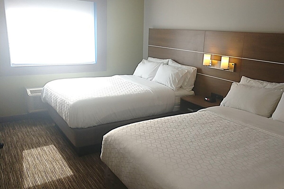 Ein Hotelzimmer mit zwei Betten, einem Nachttisch und einem Fenster mit Jalousien.