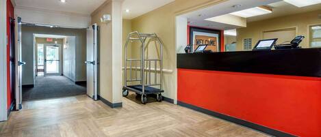 A hotel reception area with a red counter, a welcome sign, and a cart.