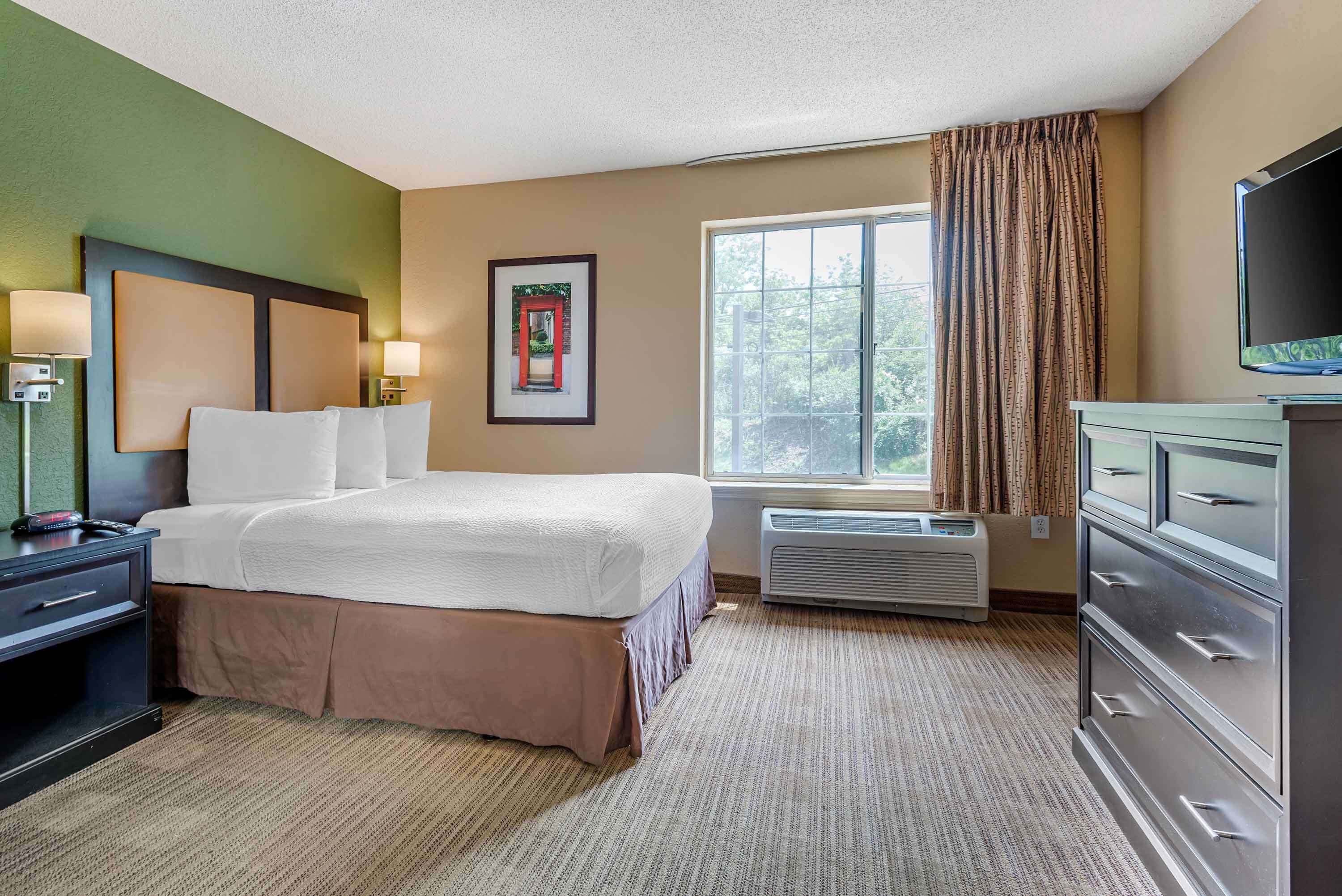 A hotel room with a bed, bedside lamps, a window with curtains, a television, and a dresser.