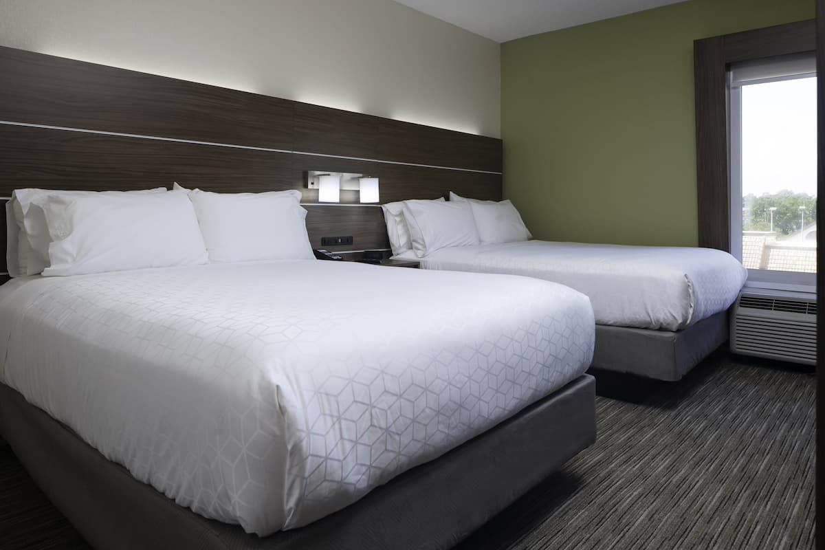 A hotel room with two beds, a nightstand, a window, and a view of the outside.
