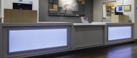 A reception area with a check-in counter, a bulletin board, and a display of amenities.