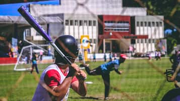 A baseball player in a white and red uniform holding a bat, with a blurred background of a sports field and spectators.