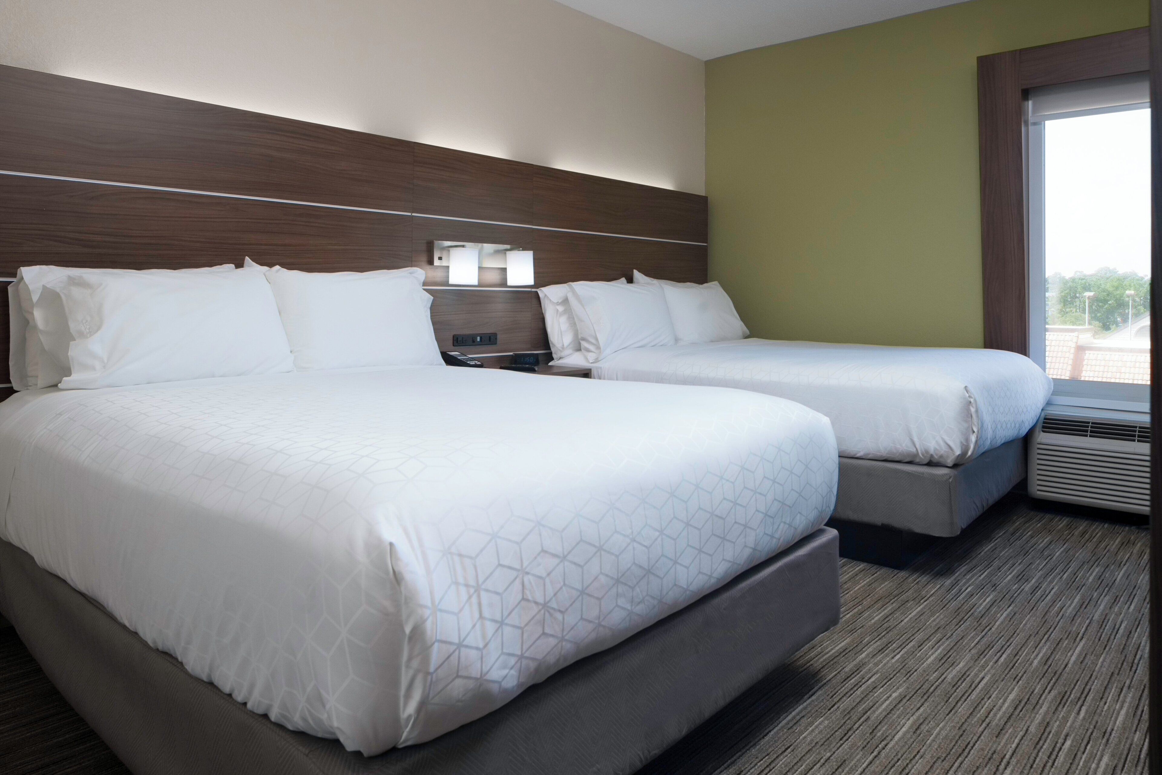 A hotel room with two beds, a nightstand, and a window with a view.