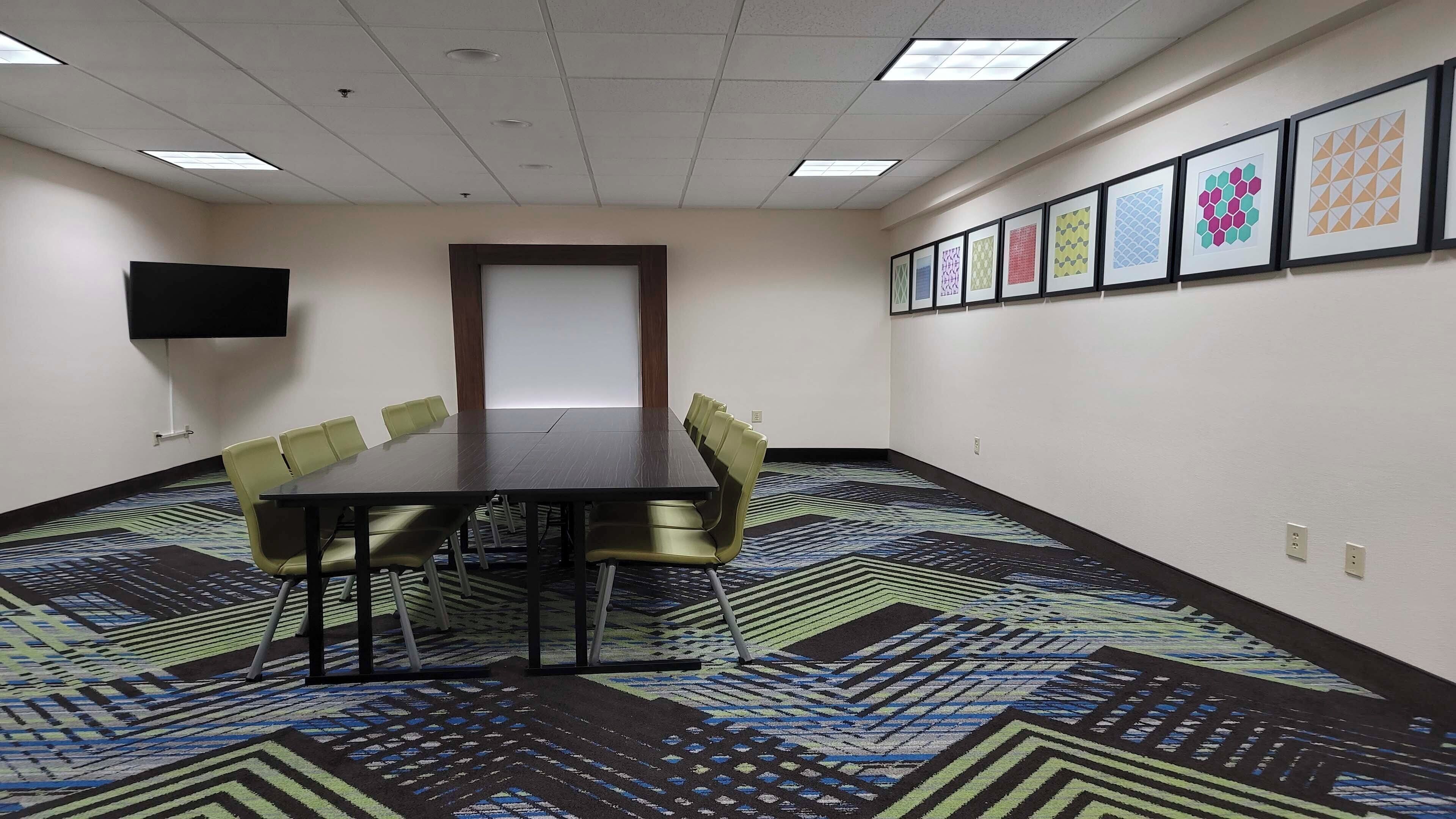Un salón de conferencias con una larga mesa, sillas, un televisor de pantalla plana y cuadros en la pared.
