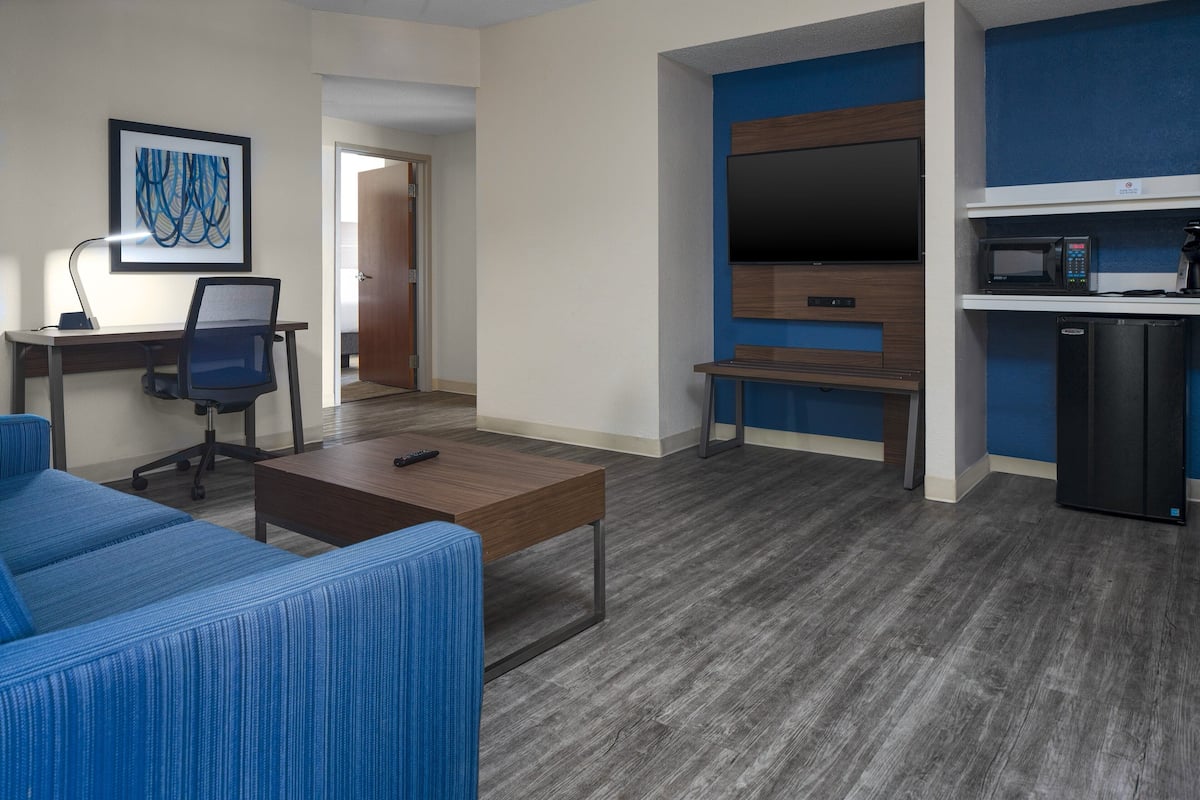 A modern living room with a sofa, a coffee table, a TV, and a kitchenette area with a microwave and refrigerator.