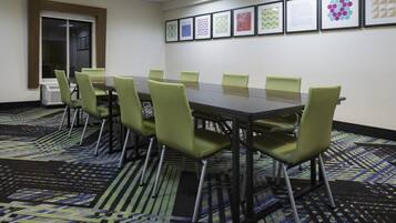 A conference room with a long table, green chairs, patterned carpet, and framed artwork on the wall.