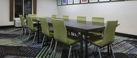 A conference room with a long table, green chairs, patterned carpet, and framed artwork on the wall.