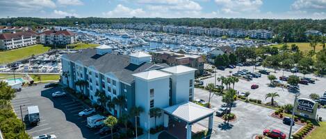 A hotel with a parking lot, a marina with boats, and a golf course in the background.