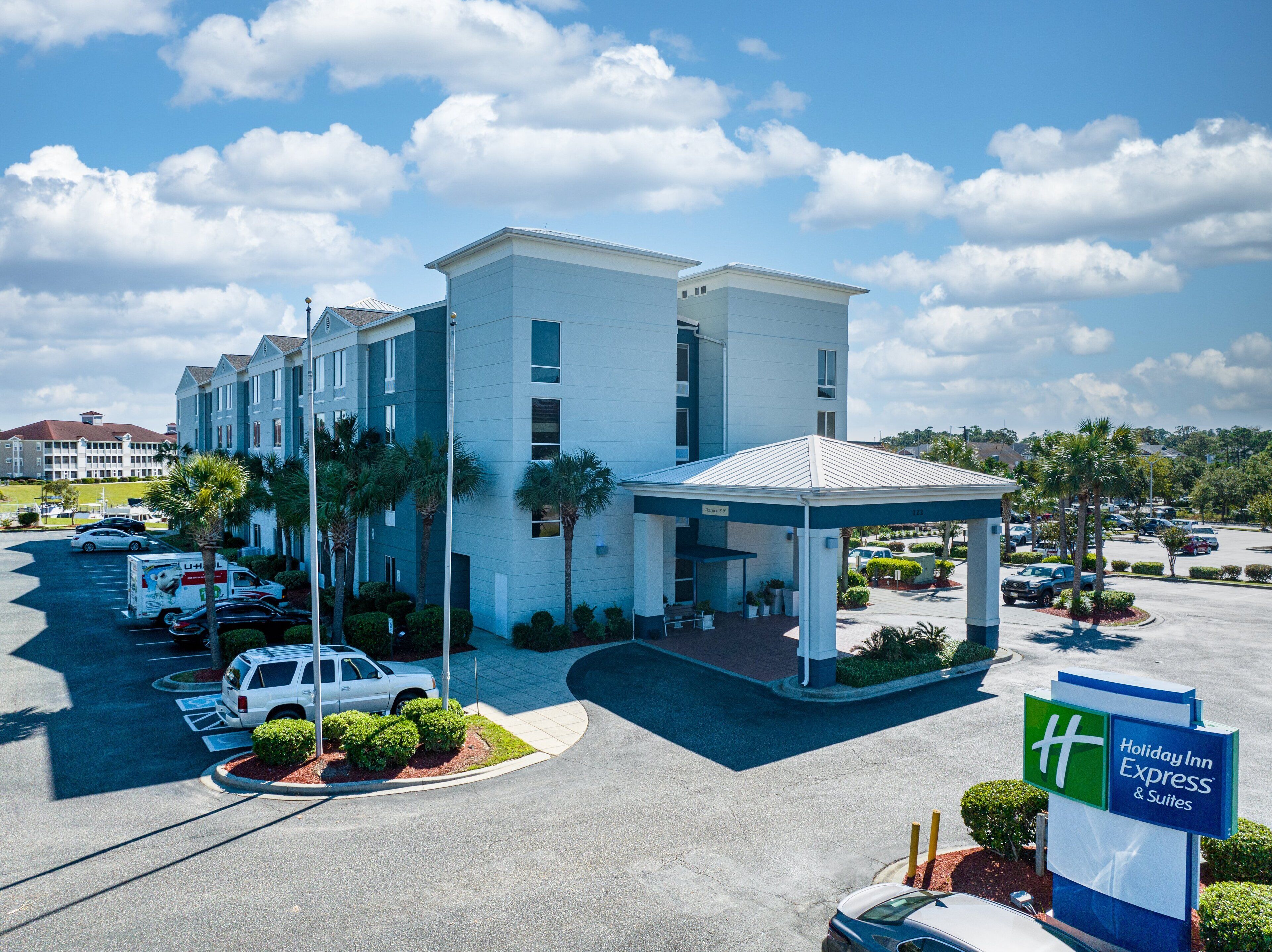 A Holiday Inn Express & Suites with a covered entrance, parking lot, and surrounding greenery.