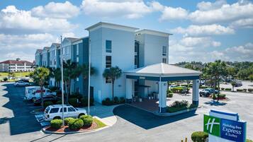 Ein Holiday Inn Express & Suites Hotel mit überdachter Zufahrt, Parkplatz und umliegender Bepflanzung.