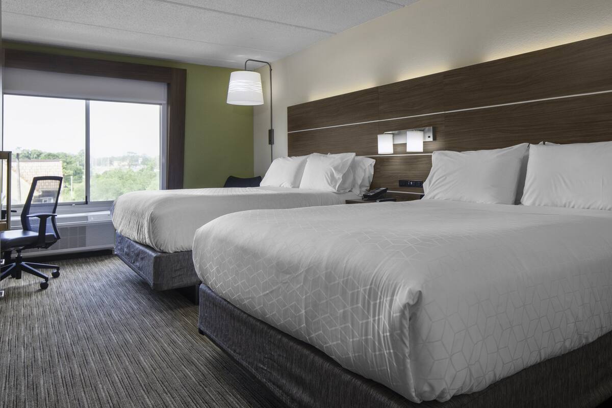 A hotel room with two beds, a desk, and a chair.