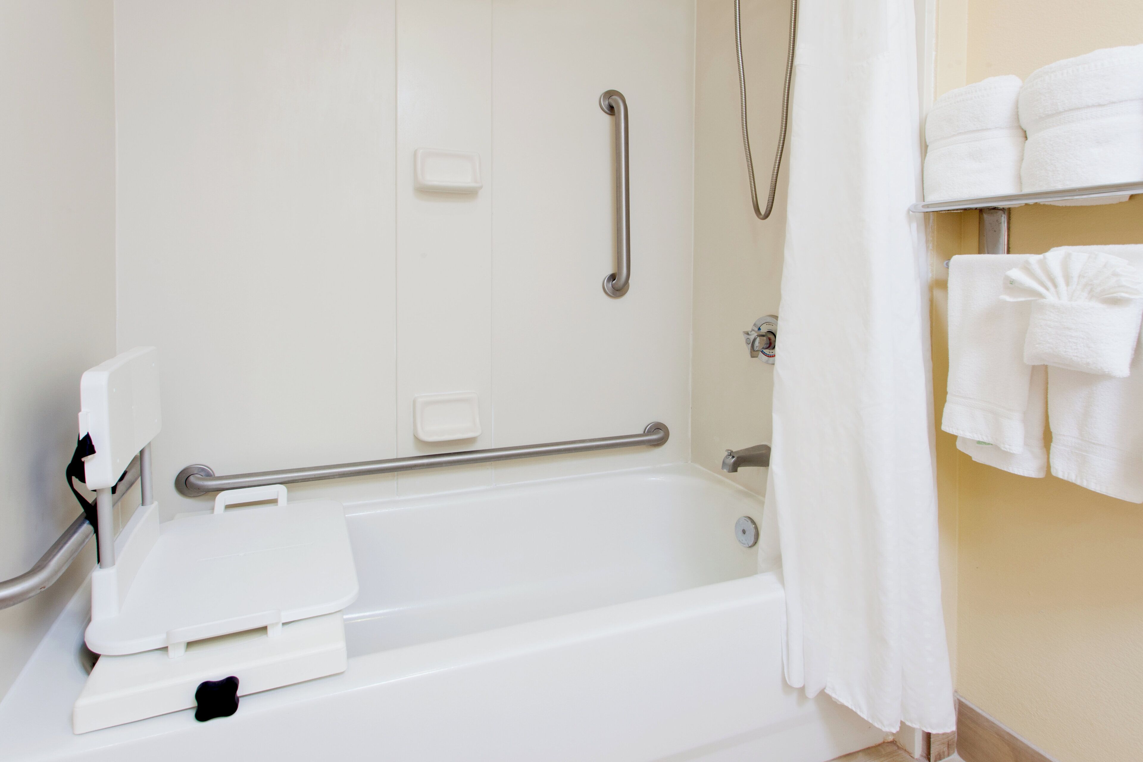 A bathroom with a white bathtub, grab bars, a shower curtain, and a towel rack with towels.