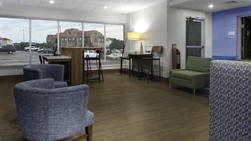 Un hall d’hôtel comprenant un comptoir d’accueil, un espace salon et de grandes fenêtres donnant sur la rue et les bâtiments environnants.