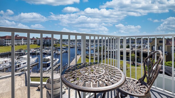 A balcony with a view of a marina, featuring a round table and two chairs. - Holiday Inn Express N.Myrtle Beach- Little River by IHG (Little River)
