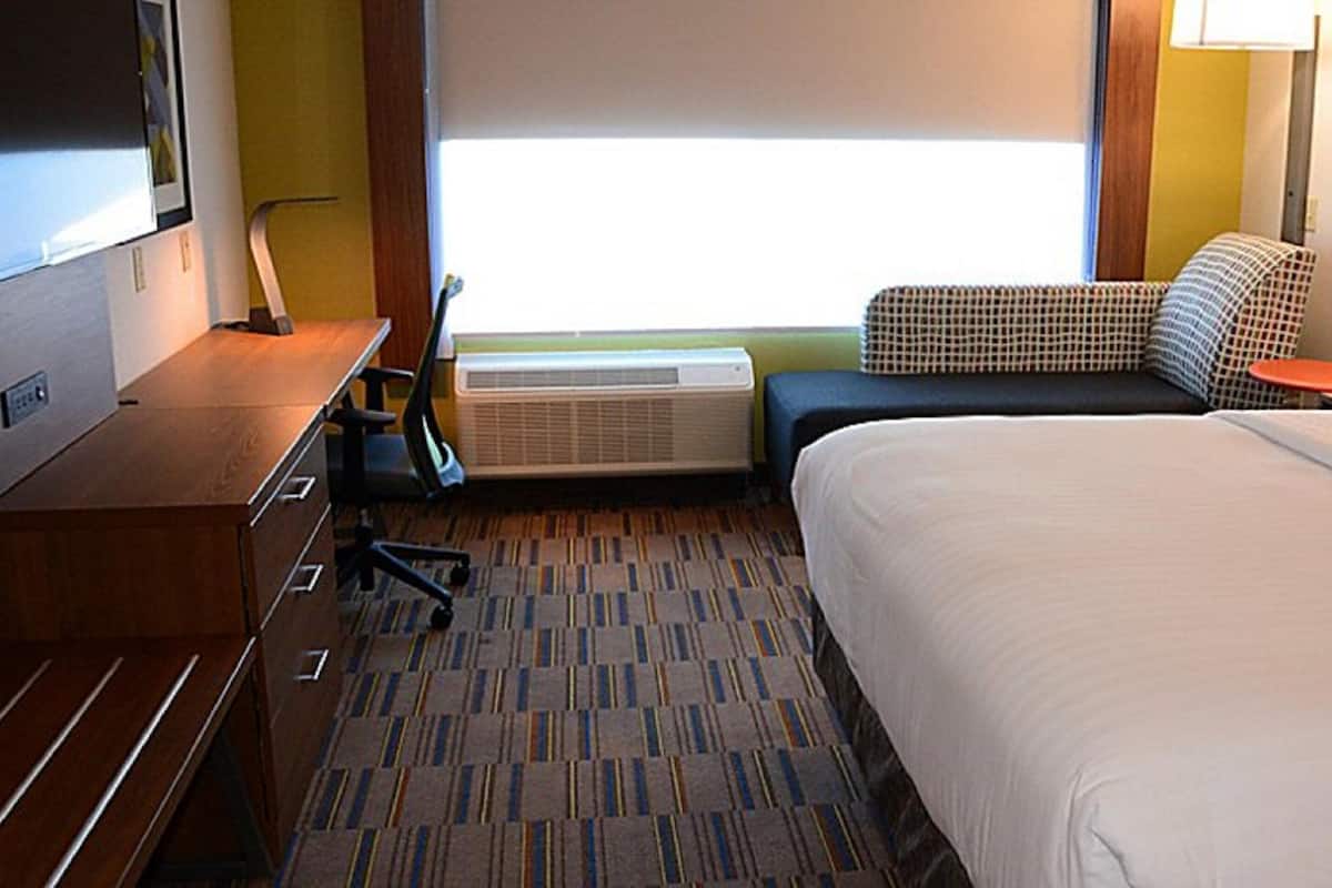 A hotel room with a bed, a desk, a chair, a small table, and a window with blinds.