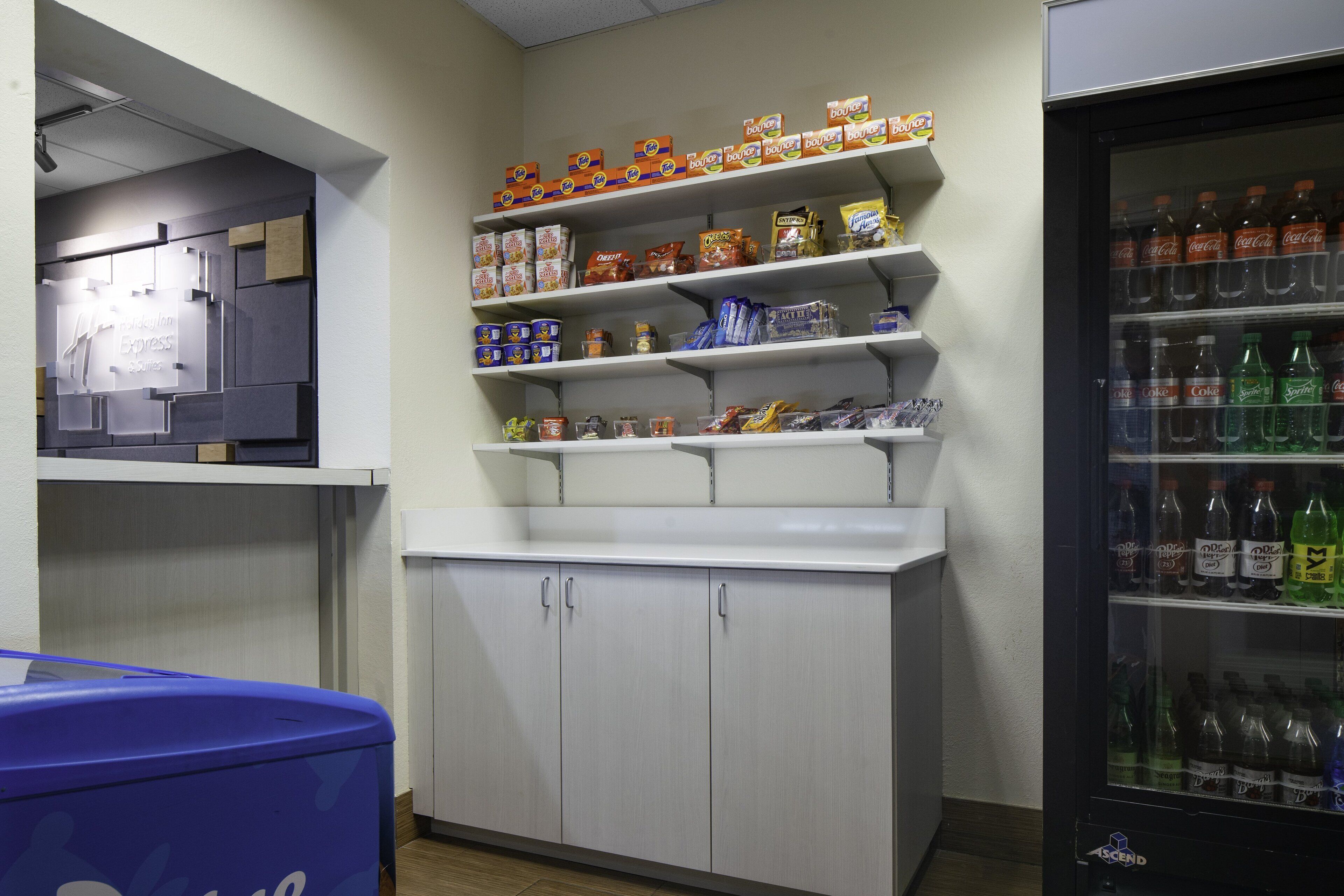 A kitchenette with shelves stocked with food items and a refrigerator with beverages.