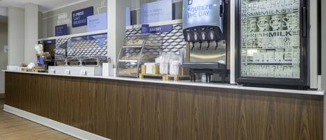 A bakery counter with a yogurt dispenser and a display of various bakery items.