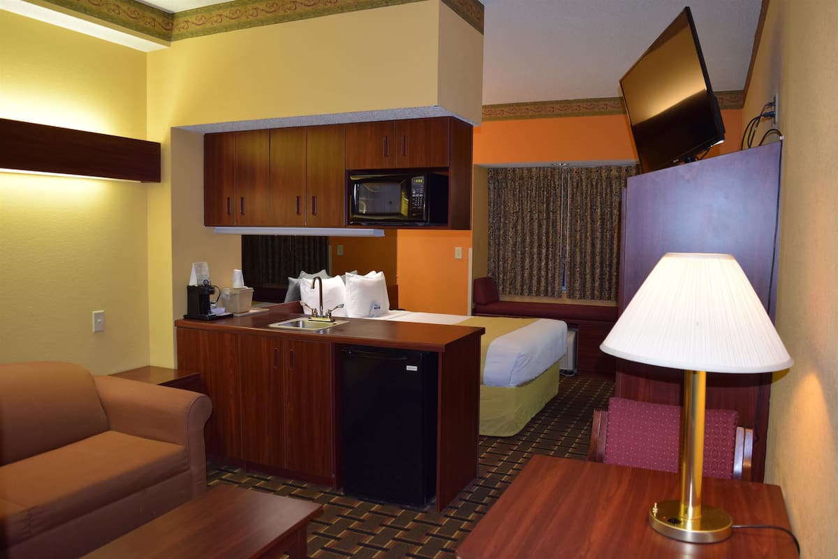 Habitació d'hotel senzilla amb cuineta, llit, escriptori i televisió penjada a la paret.