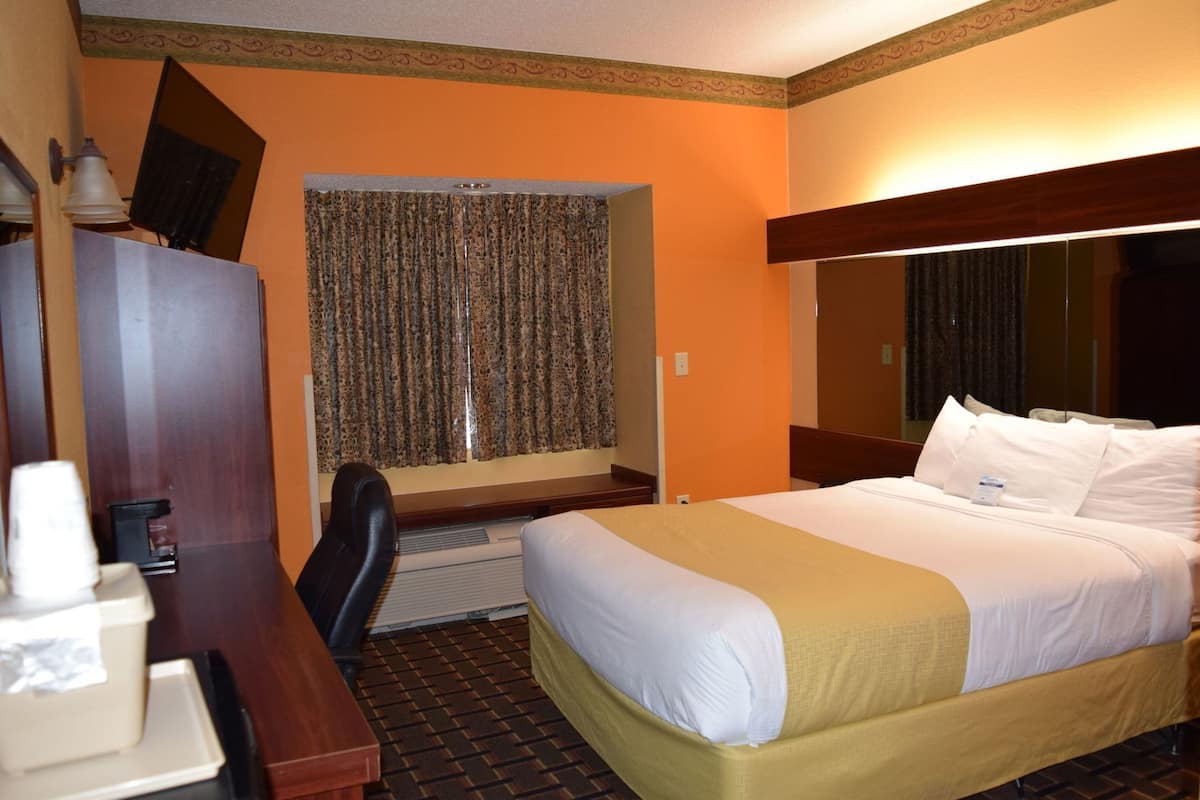 Habitació d'hotel amb un llit, escriptori, cadira i finestra amb cortines.