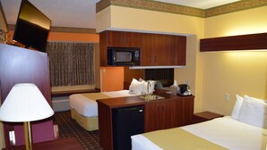 Une chambre d’hôtel comprenant un lit, un bureau avec une lampe, un four à micro-ondes, un mini-réfrigérateur et une petite kitchenette.