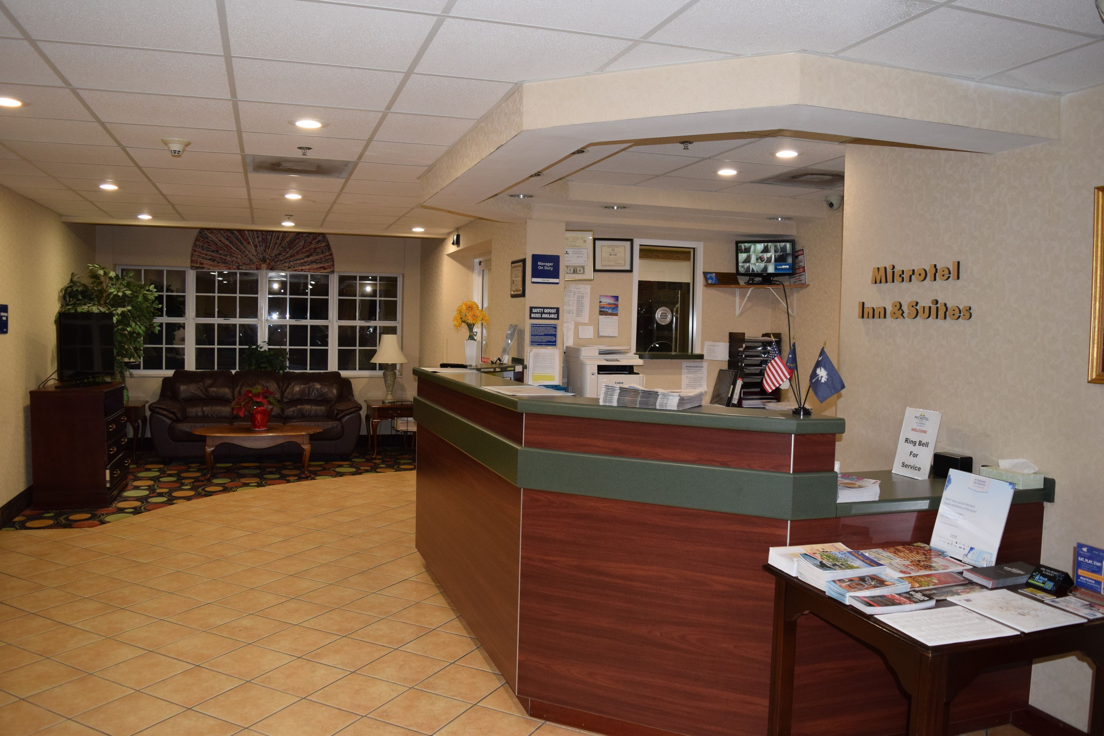 A reception area with a wooden reception desk, a sofa, and a coffee table. There are flags, a television, and framed certificates on the wall.