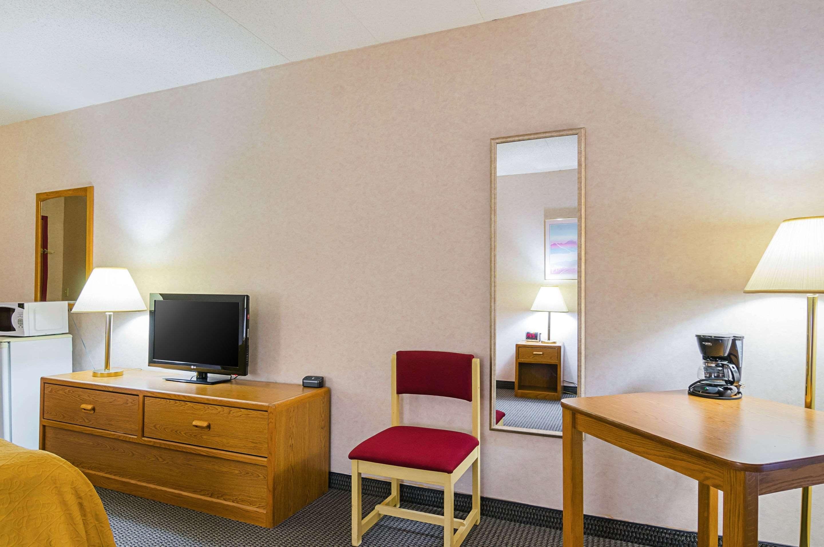 Habitación de hotel con cómoda de madera, televisor, silla roja, mesa, cafetera y espejo.