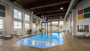 Une piscine intérieure dotée d’une structure de jeux, de grandes fenêtres et de chaises longues.