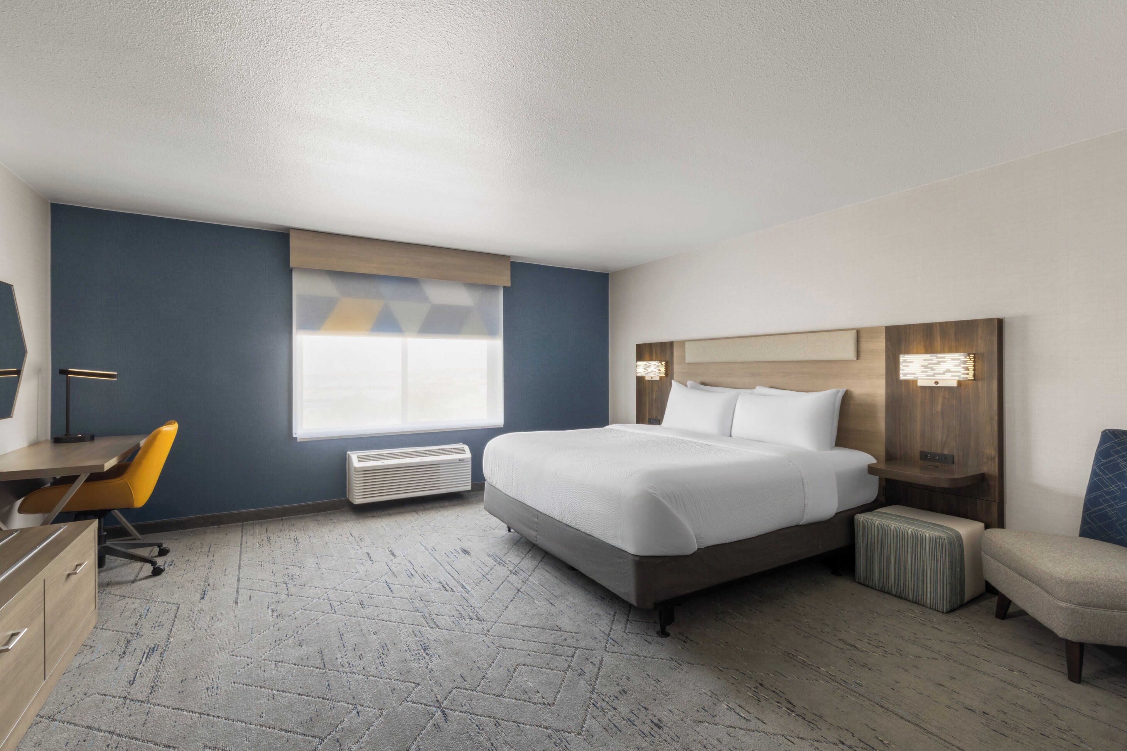 A hotel room with a bed, a desk, a chair, a nightstand, and a window.