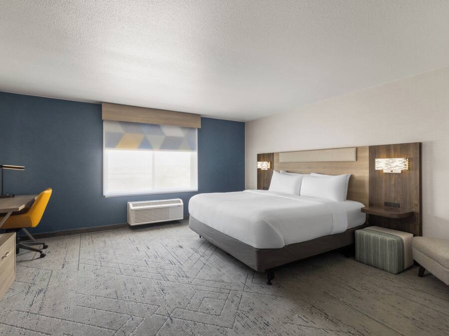 A hotel room with a bed, a desk, a chair, a nightstand, and a window.