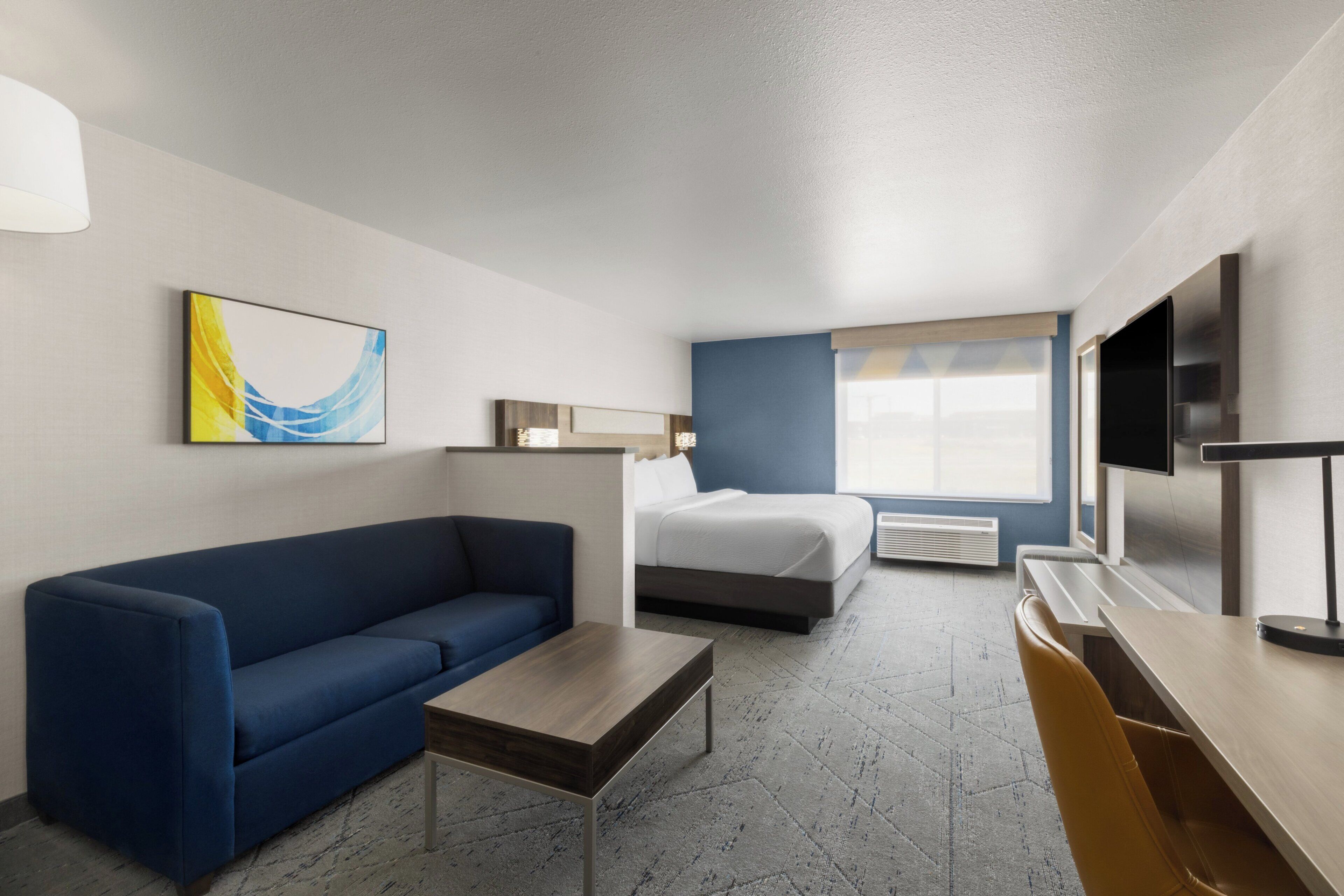 Une chambre d’hôtel avec un canapé bleu, un lit, un bureau, une télévision et une fenêtre donnant sur un paysage agréable.