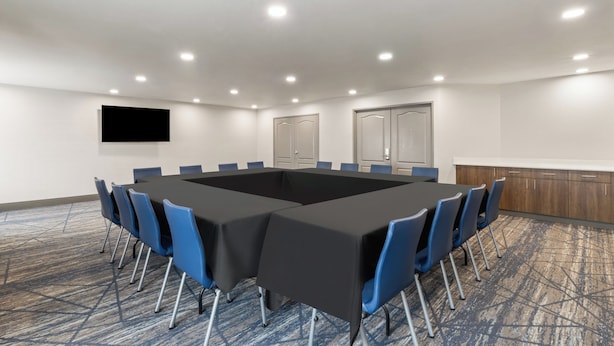 A conference room with a long table, blue chairs, a flat-screen TV, and a carpeted floor. - Holiday Inn Express Hotel & Suites Rapid City by IHG (Rapid City)