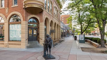 A statue on a sidewalk in front of a building with arched windows and a brick facade.