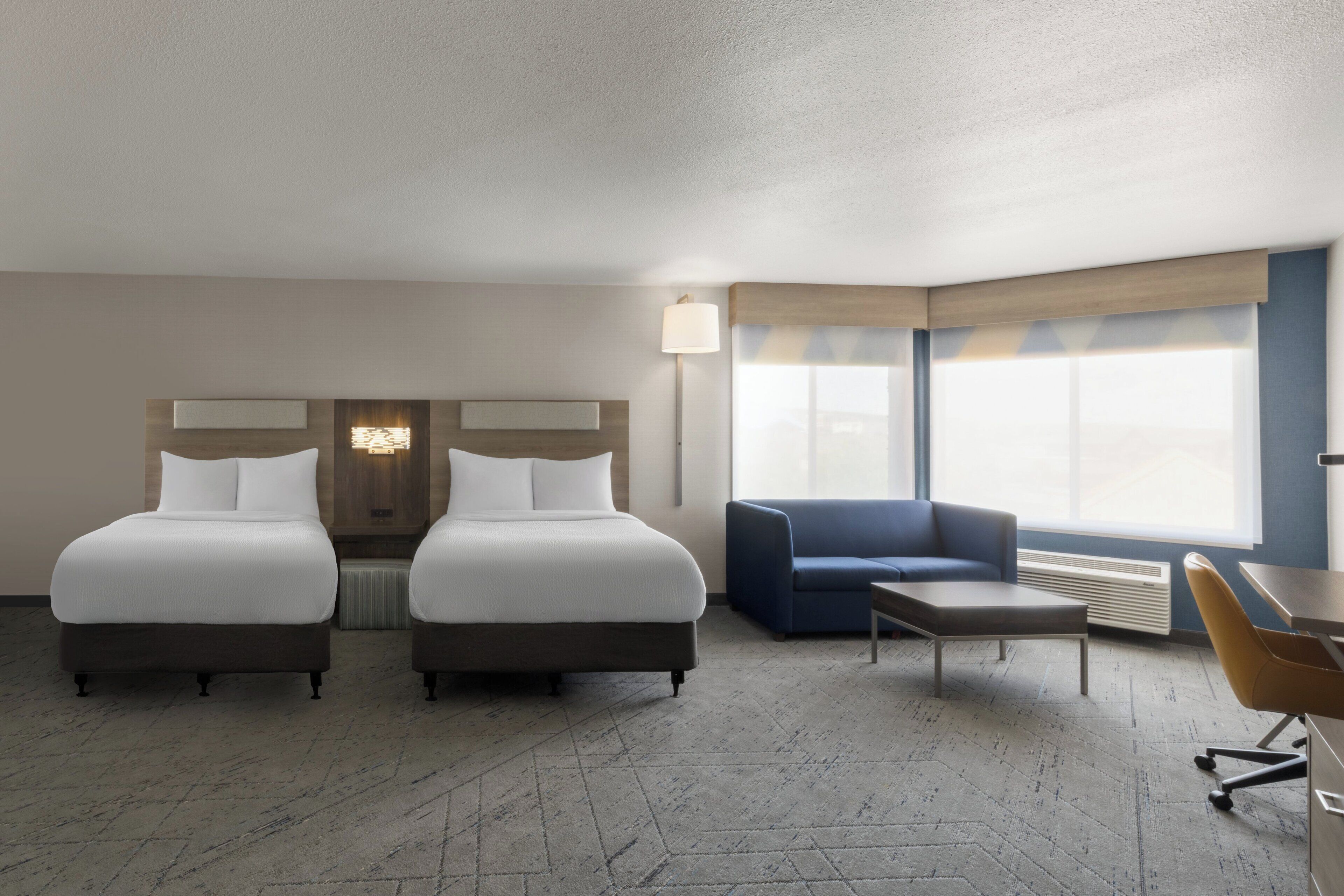 Une chambre d’hôtel avec deux lits, un canapé, un bureau et une lampe.