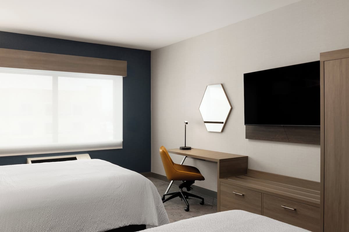 A hotel room with two beds, a desk, a chair, a TV, and a wardrobe.