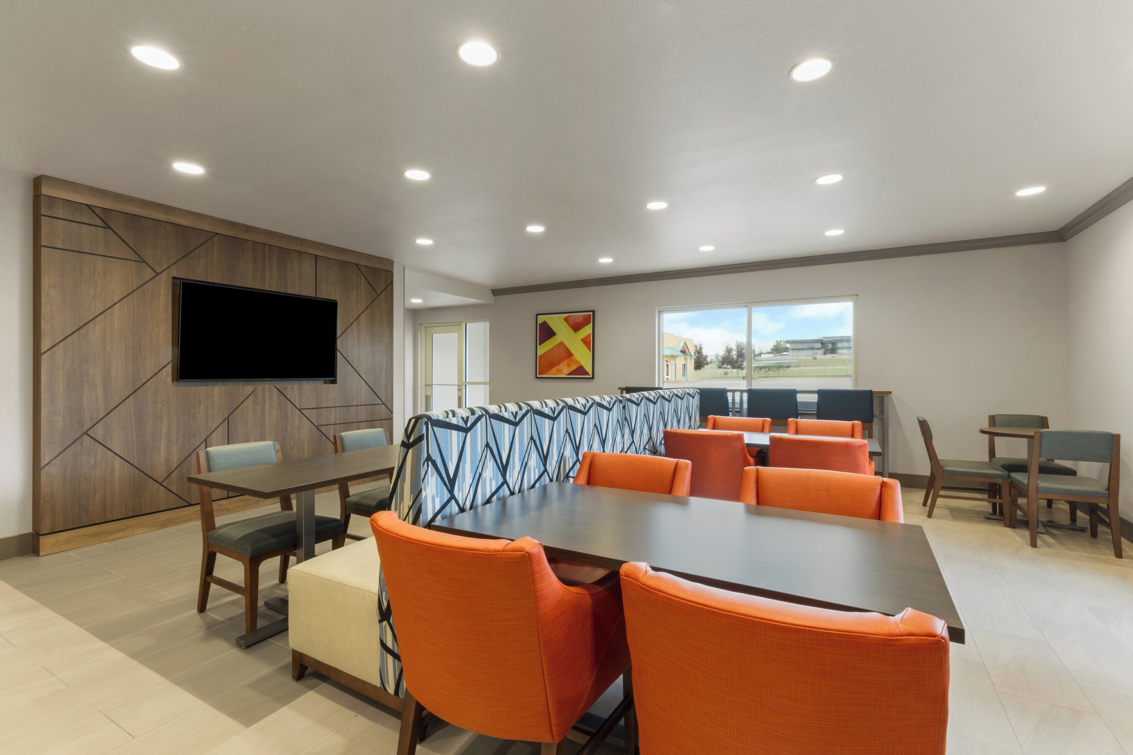 A conference room with a large table, orange chairs, a flat-screen TV, and a window with a view.