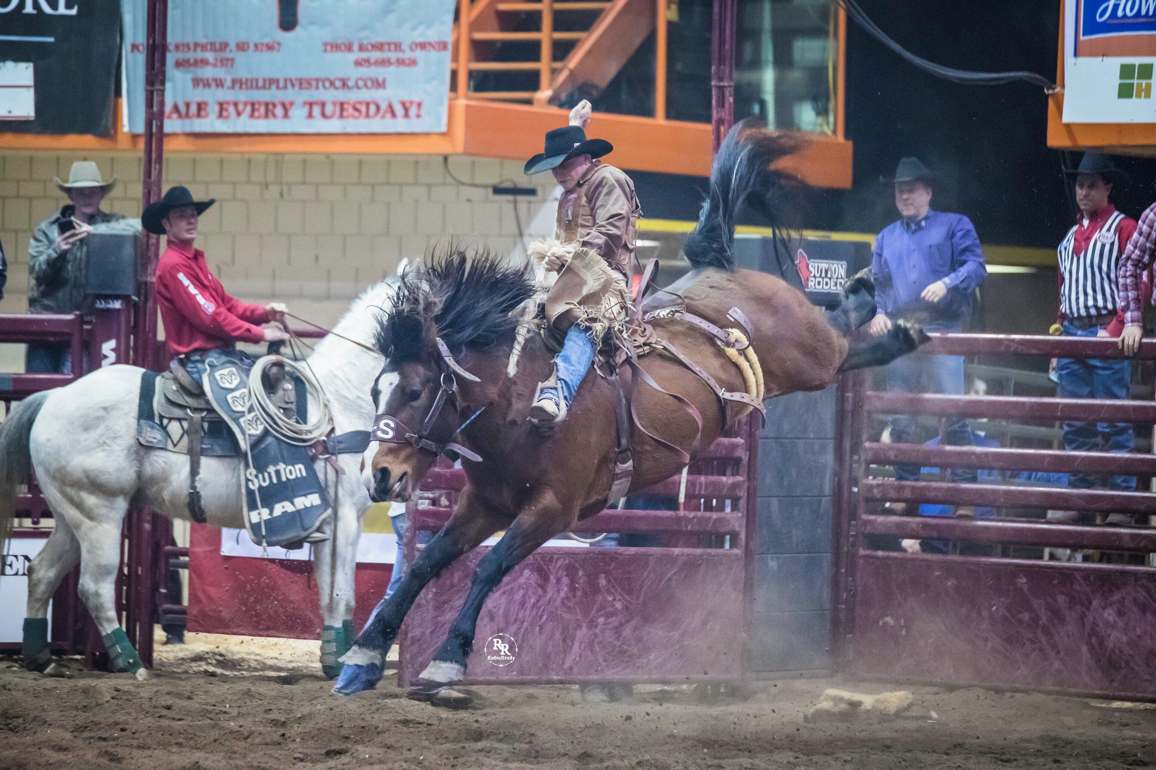 A rodeo event with a rider on a bucking horse, surrounded by spectators and other participants.