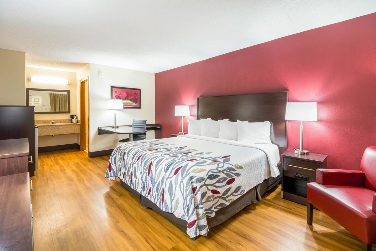 A hotel room with a bed, bedside tables, a desk, a chair, and a television.