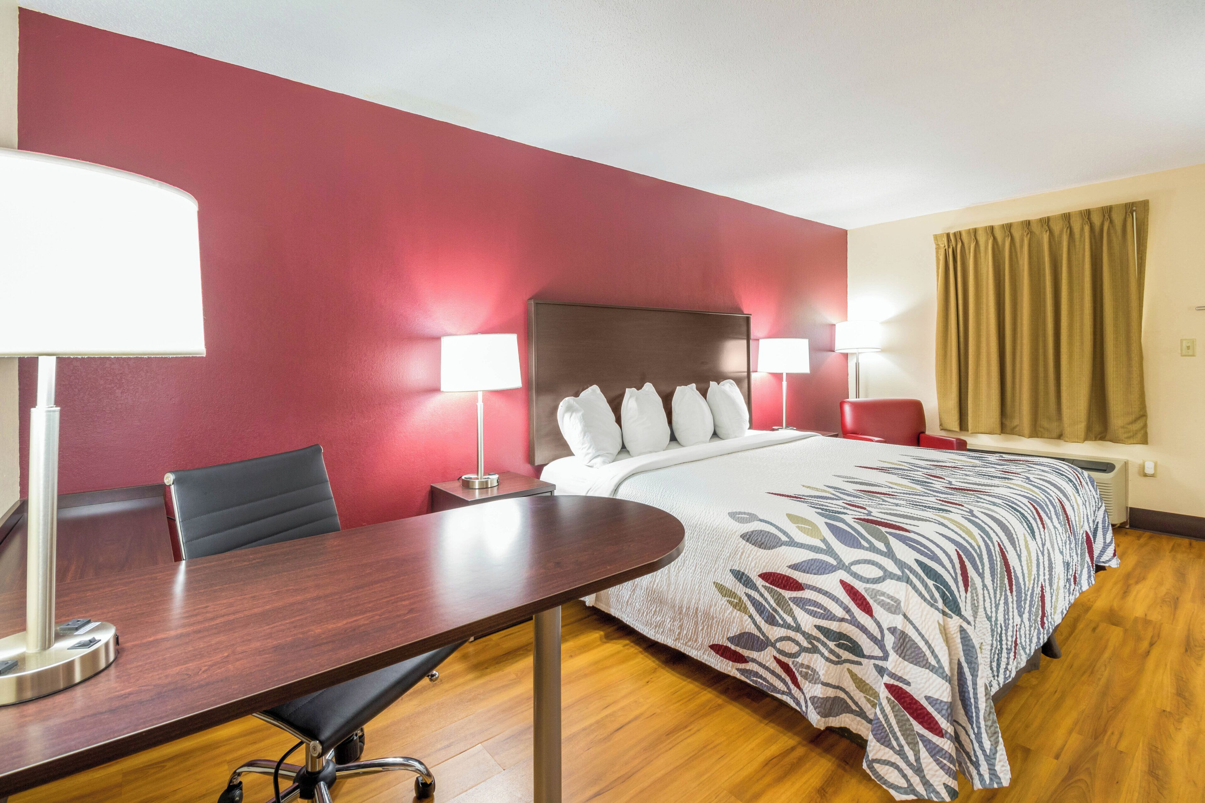 Une chambre d’hôtel avec un lit, deux lampes de chevet, un bureau avec une chaise et une fenêtre avec des rideaux.