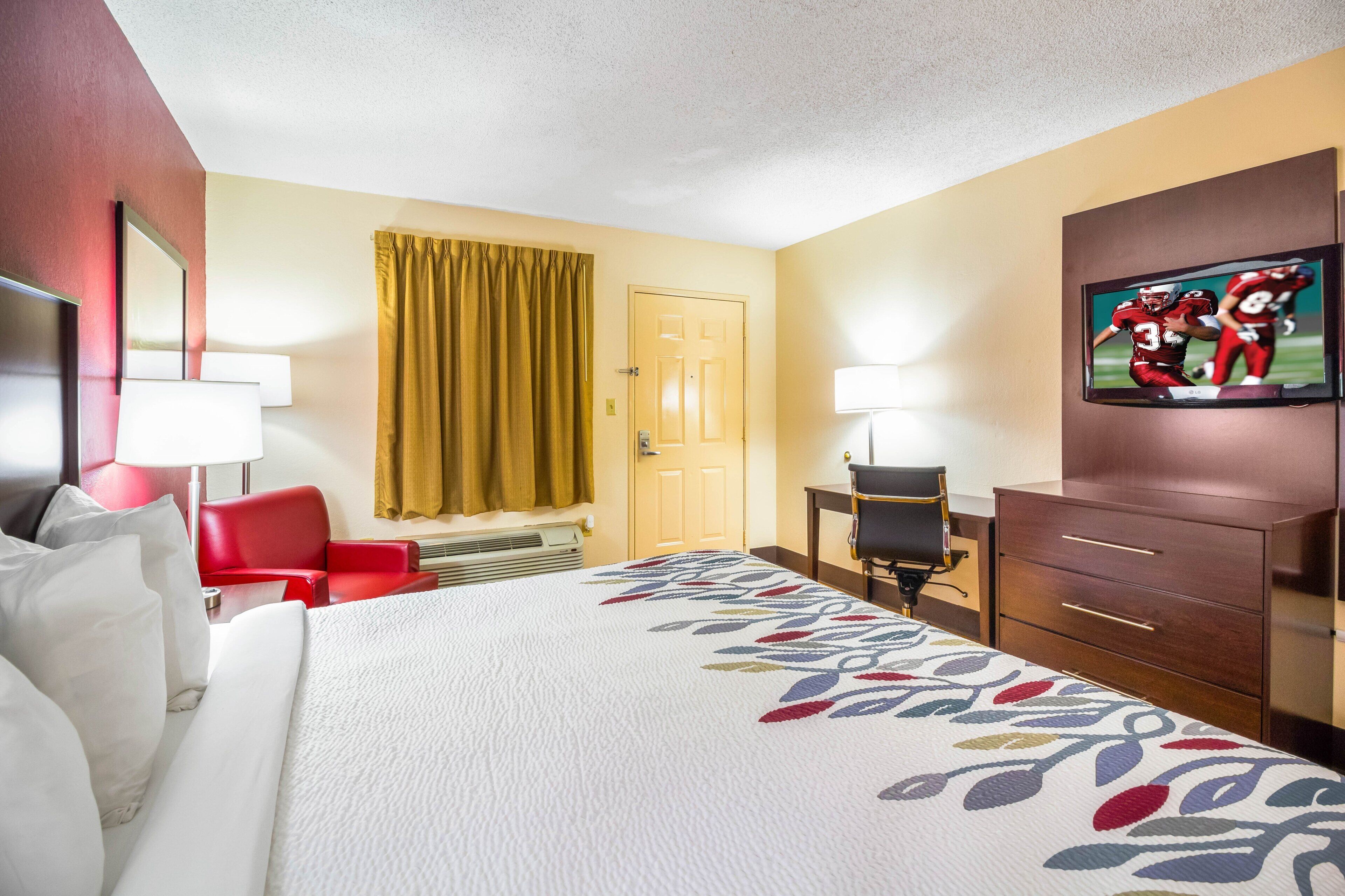 A hotel room with a bed, a desk, a chair, a TV, and a wardrobe.
