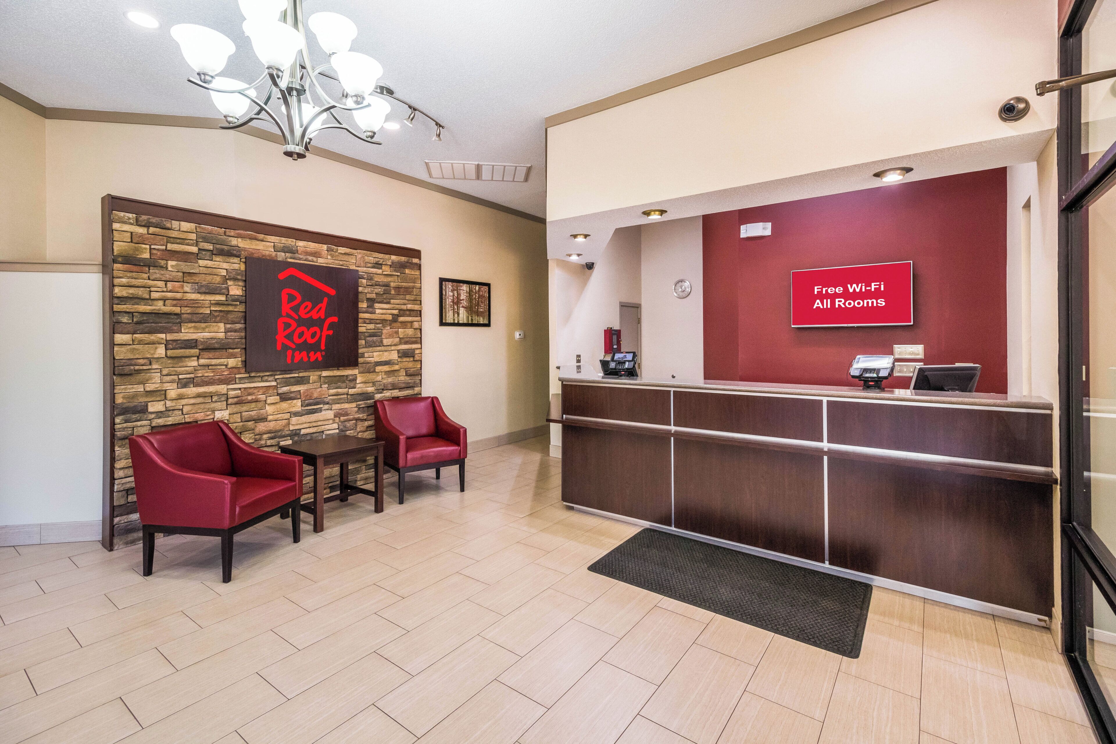 Zona de recepción de Red Roof Inn con pared de piedra, dos sillones rojos, un mostrador de recepción y un cartel que indica Wi-Fi gratuito en todas las habitaciones.