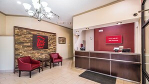A Red Roof Inn reception area with a stone wall, two red chairs, a reception desk, and a sign indicating free Wi-Fi in all rooms. - Red Roof Inn Clarksville (Clarksville)